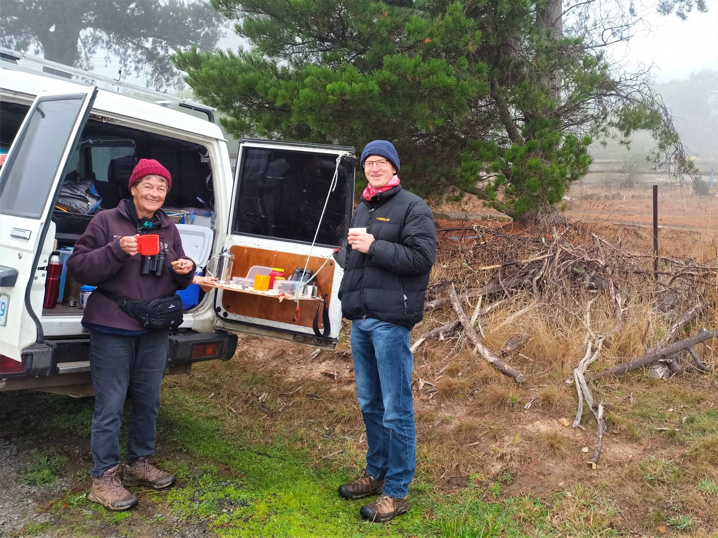 Two staunch supporters taking a well earned break, They are standing at the back of a car having a cup of tea, or maybe it’s a coffee. They are rugged up against the cold with jackets and beanies. It is a misty, cold day in Tasmania. Photo: Heidi Krajewsky.